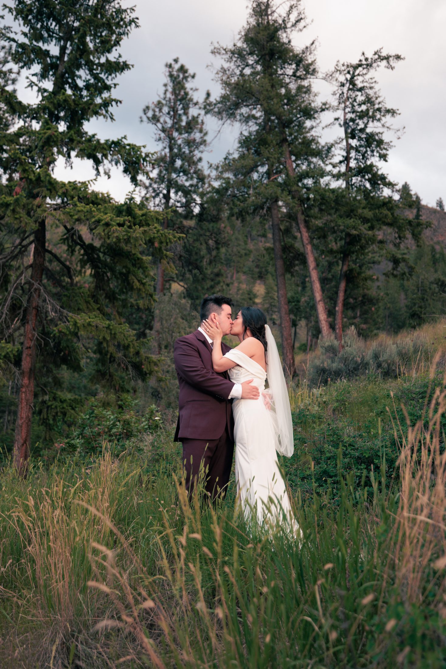 A newly married couple kissing among Okanagan pine trees
